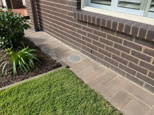 Capped access point in paved side yard beside a brick house in Epping