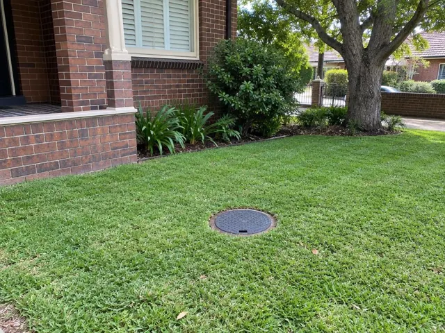 Capped sewer inspection opening in a grass lawn beside a brick house in Eastwood